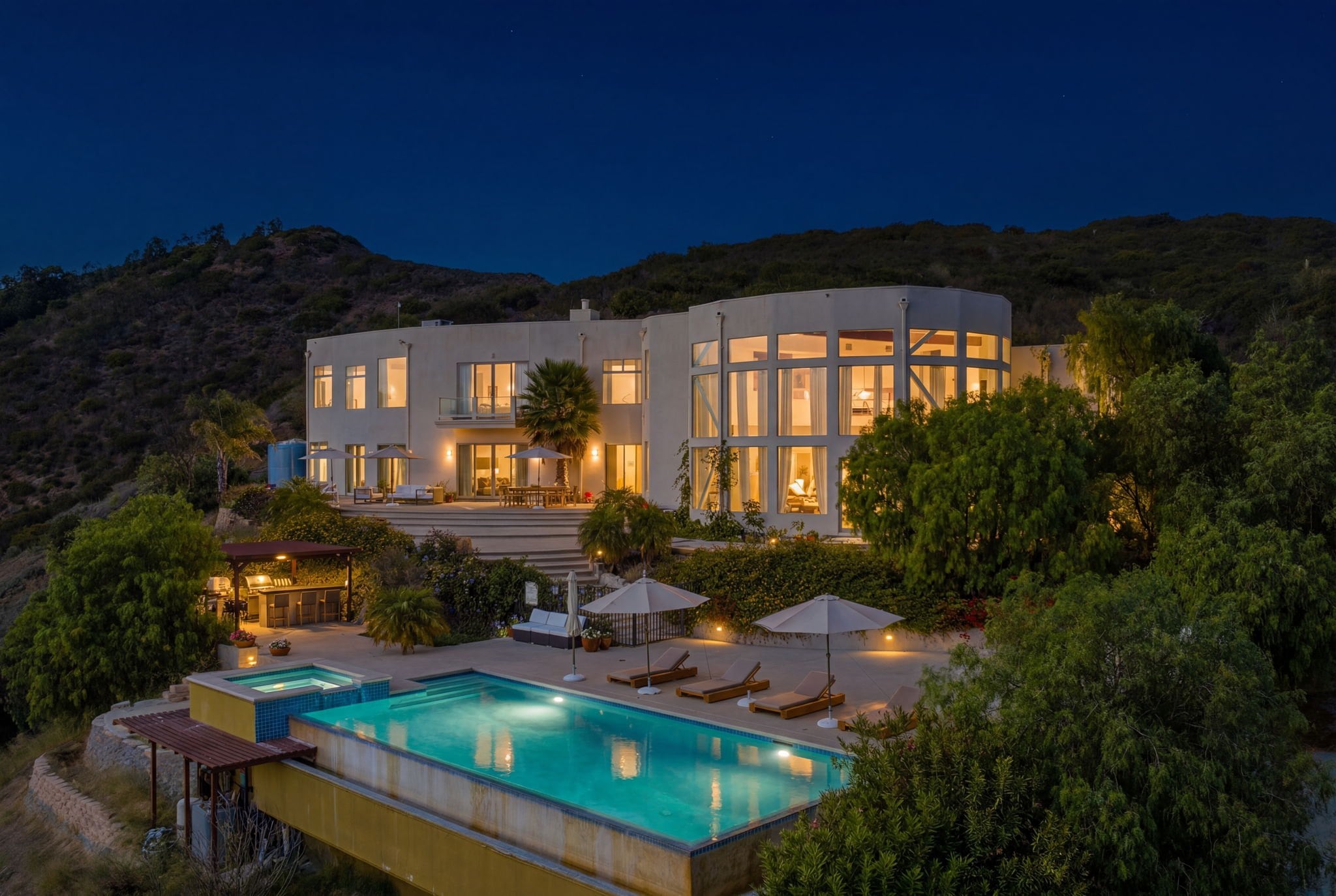 Contemporary Los Angeles hillside estate at dusk, with lit interiors and an infinity pool
